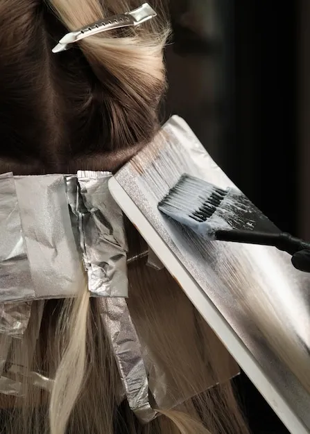 Stylist freehand painting balayage color onto long hair.