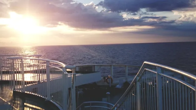 Elegant cruise ship gliding through ocean waters with passengers on sunny decks.