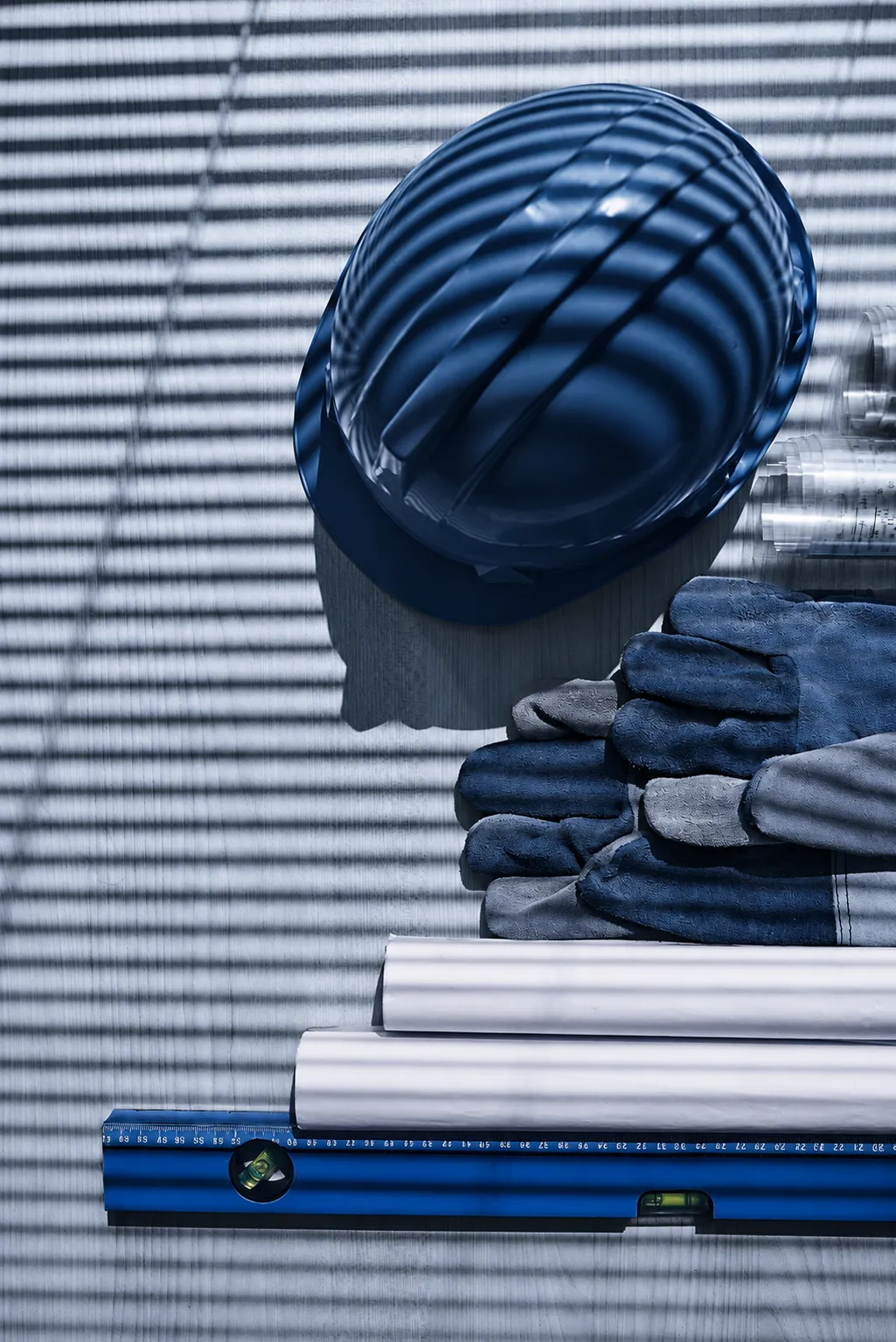 Blue hard hat, work gloves, and construction blueprints on a wooden surface.