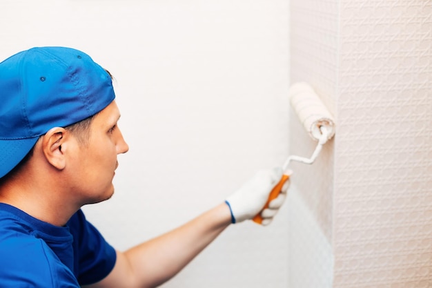 Worker painting smooth white walls in a bright apartment living room.