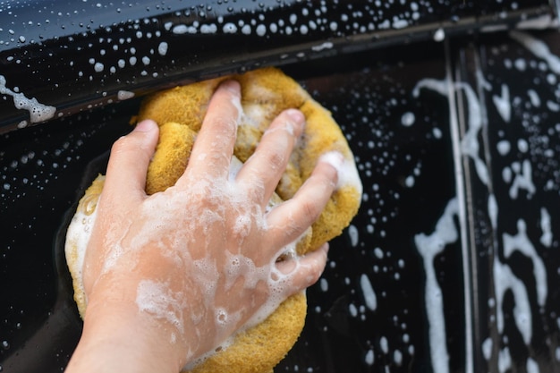 Attendant hand-washing car exterior covered in cleaning foam.