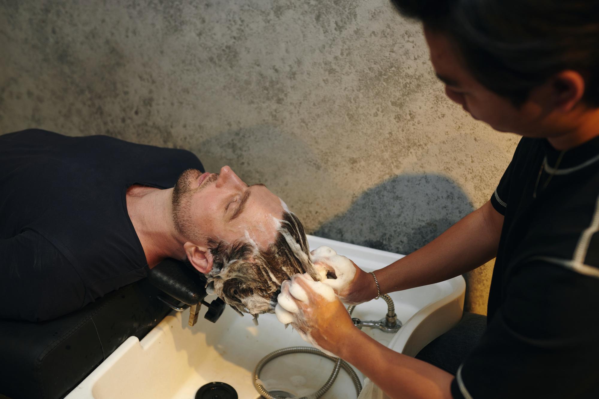 Relaxed client receiving scalp massage and treatment in barbershop.