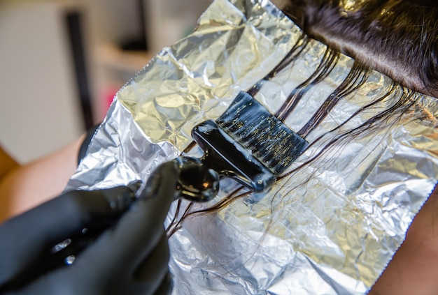 Hands placing foil sections in blonde hair for highlight application.