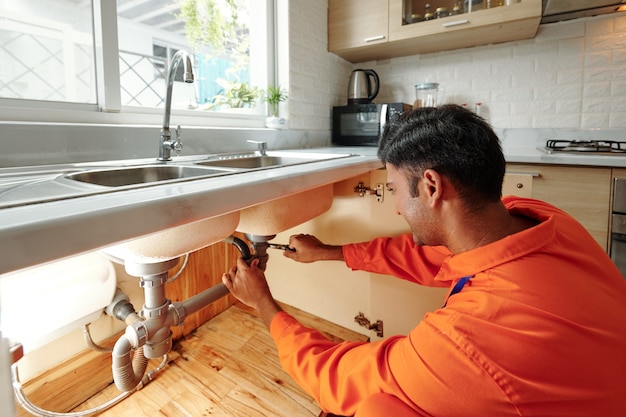 Close-up of plumber repairing a water leak on a pipe under a sink.