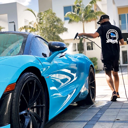 Action shot of a professional mobile detailing technician pressure washing a blue McLaren 720S.