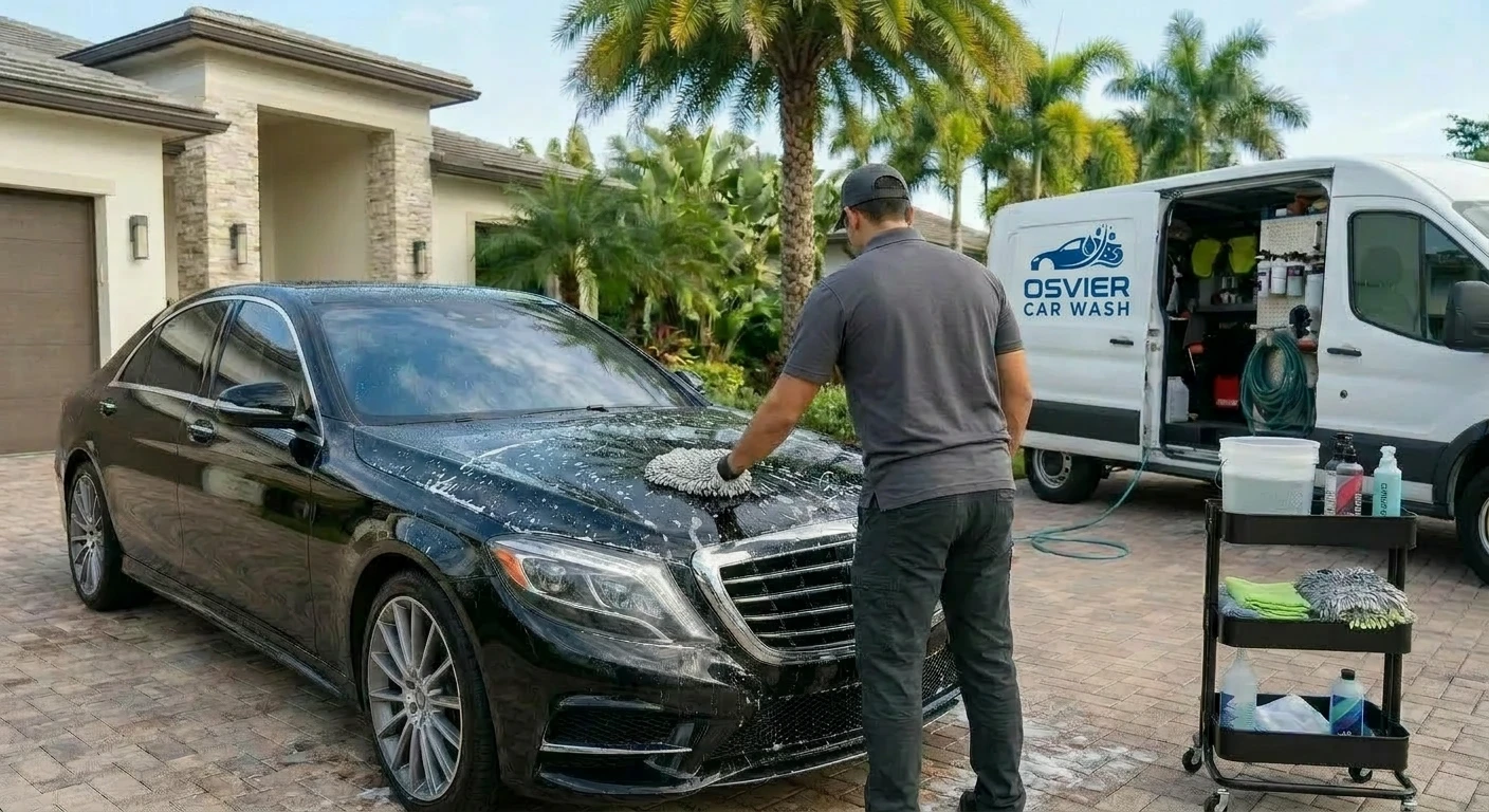 A professional detailer washing a car, facing the vehicle so only the back of their head is visible, with no branding or faces shown.
